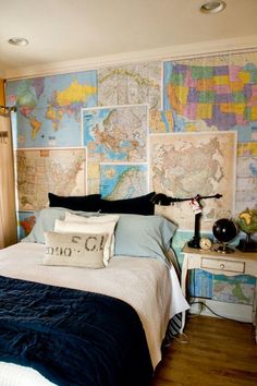 a bed sitting in a bedroom next to a wall with maps on it and a lamp