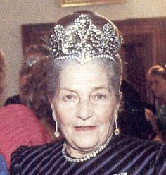 an older woman wearing a tiara in a room full of other people and looking at the camera