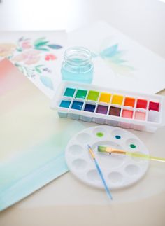 an artist's palette, watercolors and paper on a white table top