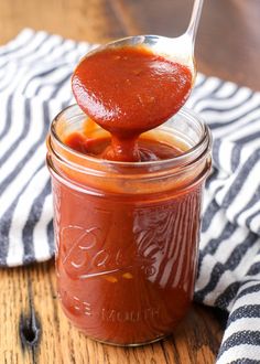 a spoon full of tomato sauce on top of a wooden table next to a black and white towel