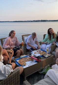 a group of people sitting on wicker chairs around a table with pizza and drinks