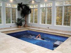 an indoor swimming pool with a person in the middle and windows on both sides that look out onto trees