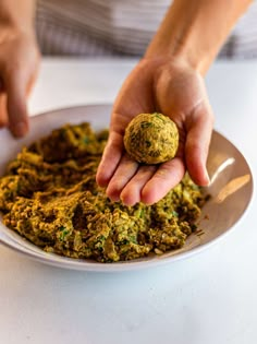 a person holding a ball in their hand over some green food on a white plate