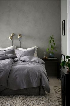 a bed with grey sheets and pillows in a room