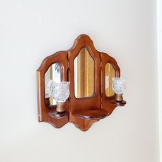 an old fashioned wooden mirror and shelf with two glass vases on it's sides