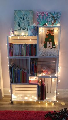 a book shelf filled with lots of books next to a red rug and christmas lights