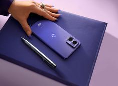 a woman's hand on the back of a purple cell phone next to a pen