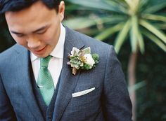 a man in a suit and green tie looking down at his cell phone while wearing a boutonniere