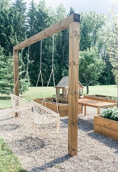 a wooden swing set with hammock and table in the back ground, surrounded by trees