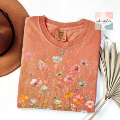 Boho Wildflower Comfort Colors Shirt, Wildflowers Cottagecore Shirt, Boho Wildflower Tshirt, Floral Botanical Shirt Women, Flower Garden Lover Gift  ❤ Comfort Colors® Brand Shirts & Unisex Adult Sizing The softly washed, garment-dyed fabric adds extra comfort to your wardrobe, and its relaxed fit makes it a great everyday choice. The shirt's double-needle stitching enhances its durability, and the absence of side seams helps it maintain its tubular shape. ❤ Please note that the rolled sleeves in Wildflower Pocket Shirt Embroidered, Orange Floral Print Shirt For Spring, Orange Floral Print Cotton Shirt, Orange Cotton Floral Print Shirt, Orange Short Sleeve Tops With Floral Embroidery, Orange Floral Embroidery Short Sleeve Tops, Orange Floral Embroidered Short Sleeve Tops, Summer Crew Neck Top With Watercolor Print, Casual Cotton Tops With Watercolor Print