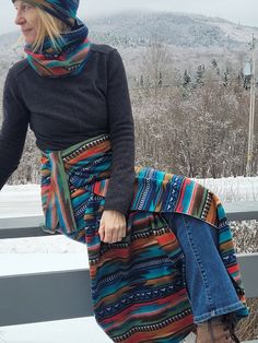 a woman sitting on top of a wooden bench wearing a colorful skirt and scarf over her head