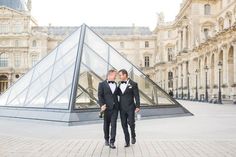 two men in tuxedos standing next to each other near a pyramid shaped building