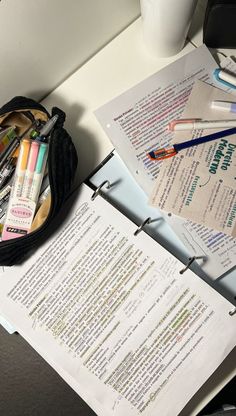 an open book on a desk next to some pens and paper with writing utensils