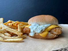 a chicken sandwich with cheese and fries on a paper towel next to a blue wall