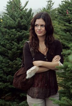 a woman standing in front of a christmas tree holding her hand on her shoulder and looking at the camera