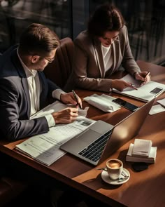 two people sitting at a table with laptops and papers