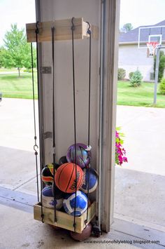 basketballs and other sports balls are hanging from a rack in front of a garage door