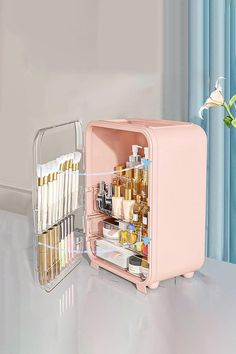 an open pink refrigerator sitting on top of a counter next to a vase with flowers