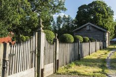 an old wooden fence with topiary bushes on it and a house in the background