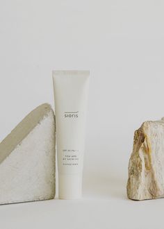 a tube of cream sitting next to a rock and piece of wood on a white background