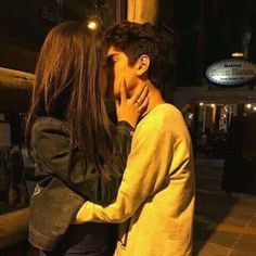 a young man and woman kissing in front of a store window at night with the lights on