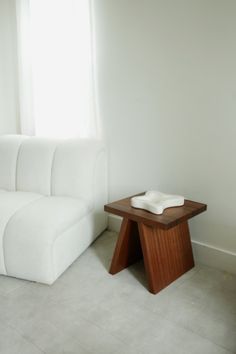 a white couch sitting next to a wooden table in a living room under a window