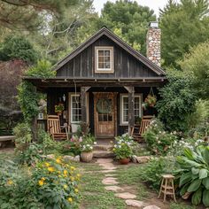 a small house with lots of flowers and plants around it's front door, surrounded by greenery