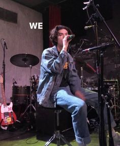 a man sitting on top of a stool singing into a microphone