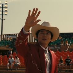 a man in a red suit and cowboy hat waves to the crowd