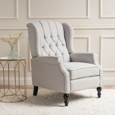 a white chair sitting on top of a rug next to a glass table and vase