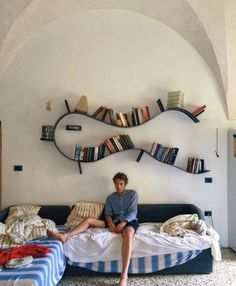 a man sitting on top of a bed next to a book shelf filled with books