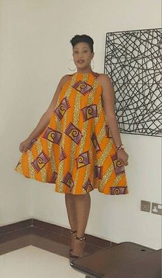 a woman standing in front of a wall wearing an orange and yellow dress with geometric designs on it