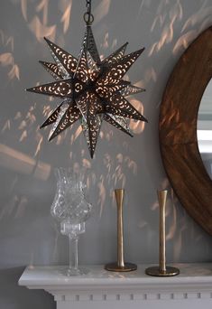 a star shaped light hanging from the ceiling next to a mirror and candle holder on a mantle