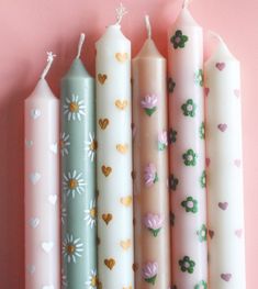 four candles are lined up against a pink wall with hearts and flowers painted on them