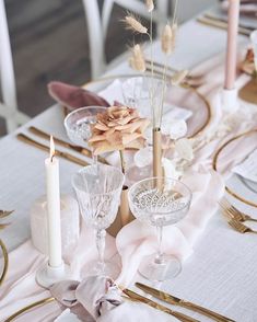 the table is set with gold and white plates, silverware, candles, and pink napkins