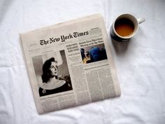 a newspaper with a cup of coffee next to it on a white sheeted surface