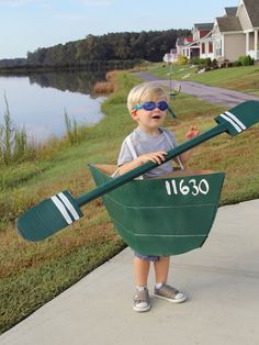 a young boy wearing sunglasses and holding a green boat shaped like a oarset