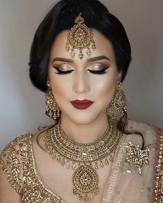 a woman wearing gold jewelry and makeup looks down at the camera with her eyes closed