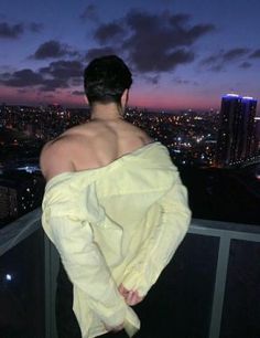 a man wrapped in a towel looks out over the city at night from his balcony