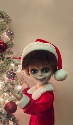 a close up of a doll near a christmas tree with ornaments on it's head