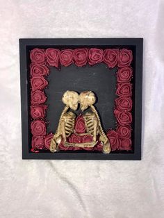 two skeletons sitting next to each other in a black frame with red roses on it