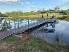 two people standing on a bridge over a body of water with grass and trees in the background