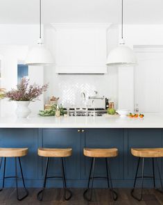 three stools sit in front of an island with blue cabinets and white countertops