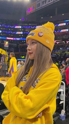 a girl in a yellow jacket and hat at a basketball game with her arms crossed