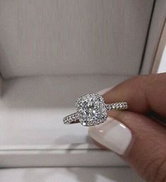 a woman's hand holding a diamond ring in front of a white box with an engagement band on it