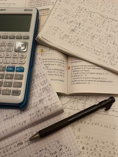 a calculator, pen and notebooks on top of paper with numbers written in it