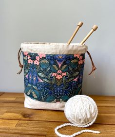 a ball of yarn next to a bucket with knitting needles in it on a wooden table