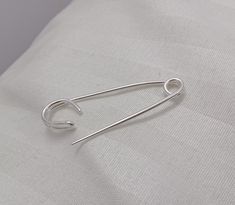 a pair of silver earrings sitting on top of a white pillow