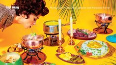 a woman blowing out candles on a table full of food and dishes, with palm trees in the background