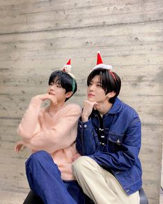 two young men sitting next to each other on a bench wearing christmas hats and sweaters